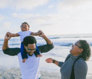 Young son on his dad's shoulders at the beach with his mom. Our St Petersburg, FL family therapist can provide support to those going through divorce or dealing with blended families. Call today to get started with family therapy to improve your household dynamics.