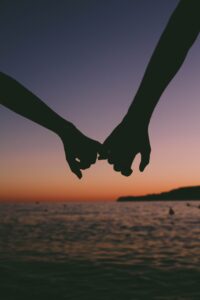 Two partners hands holding each other by one finger on the beach at sunset. Relationship therapy with a couples therapist could be the start for a success future. Call now to learn how a marriage counselor in St Petersburg, FL can support you.