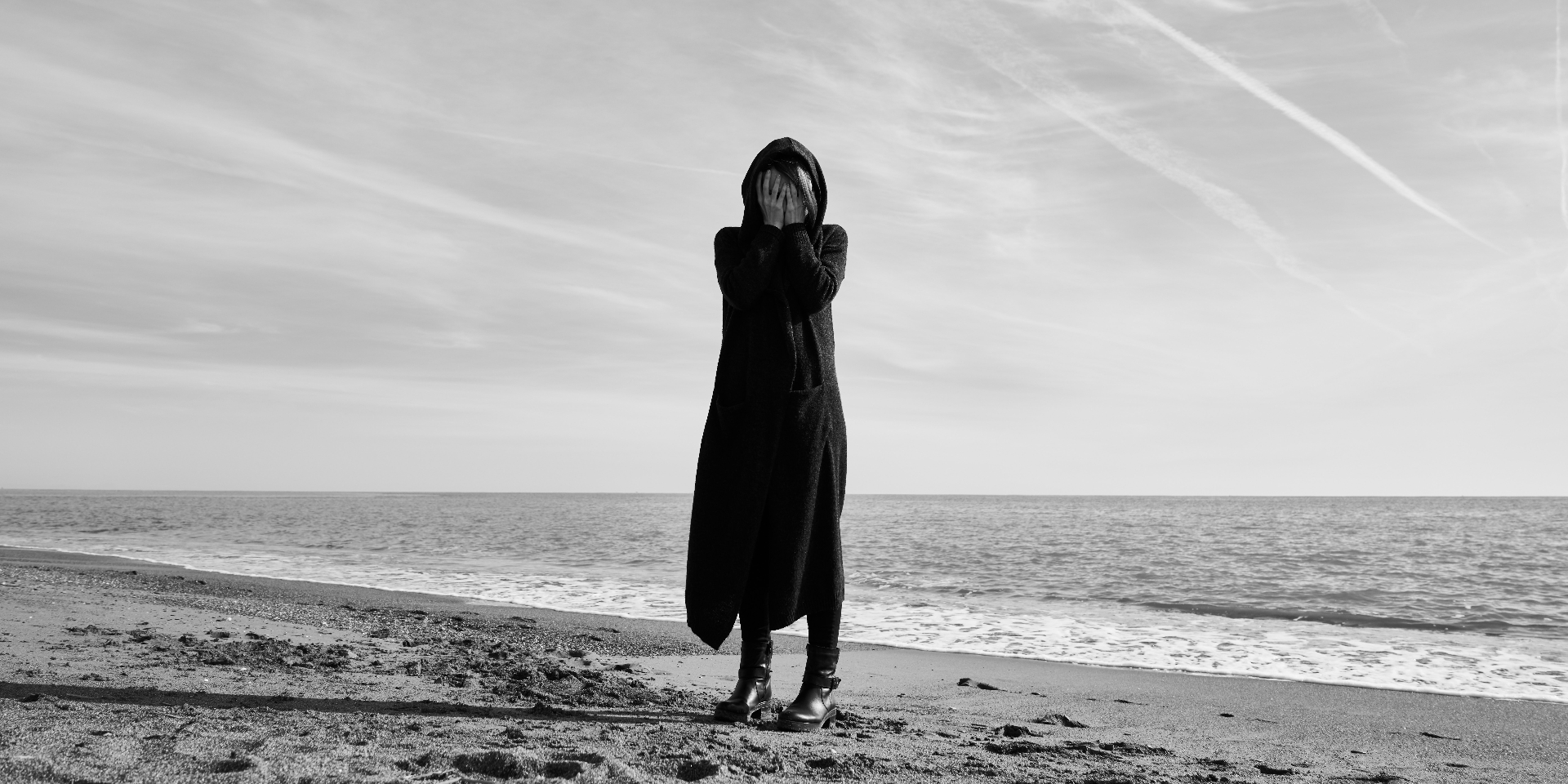 Image of a woman wearing black and covering her face while standing on a beach. Depression can be overwhelming to manage alone. Learn how depression therapy in Saint Petersburg, FL can help you cope with your symptoms.