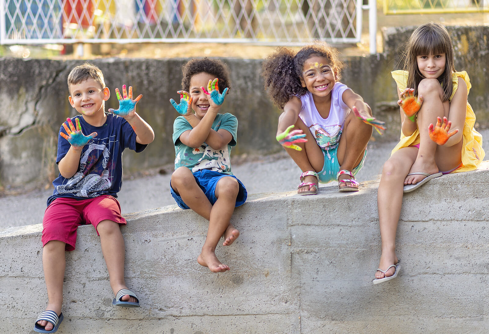 Image of four children sitting on a concrete wall outside holding up their painted hands and smiling. Do you find that your child has unique needs? Learn to support them with child neuropsych testing in Saint Petersburg, FL.