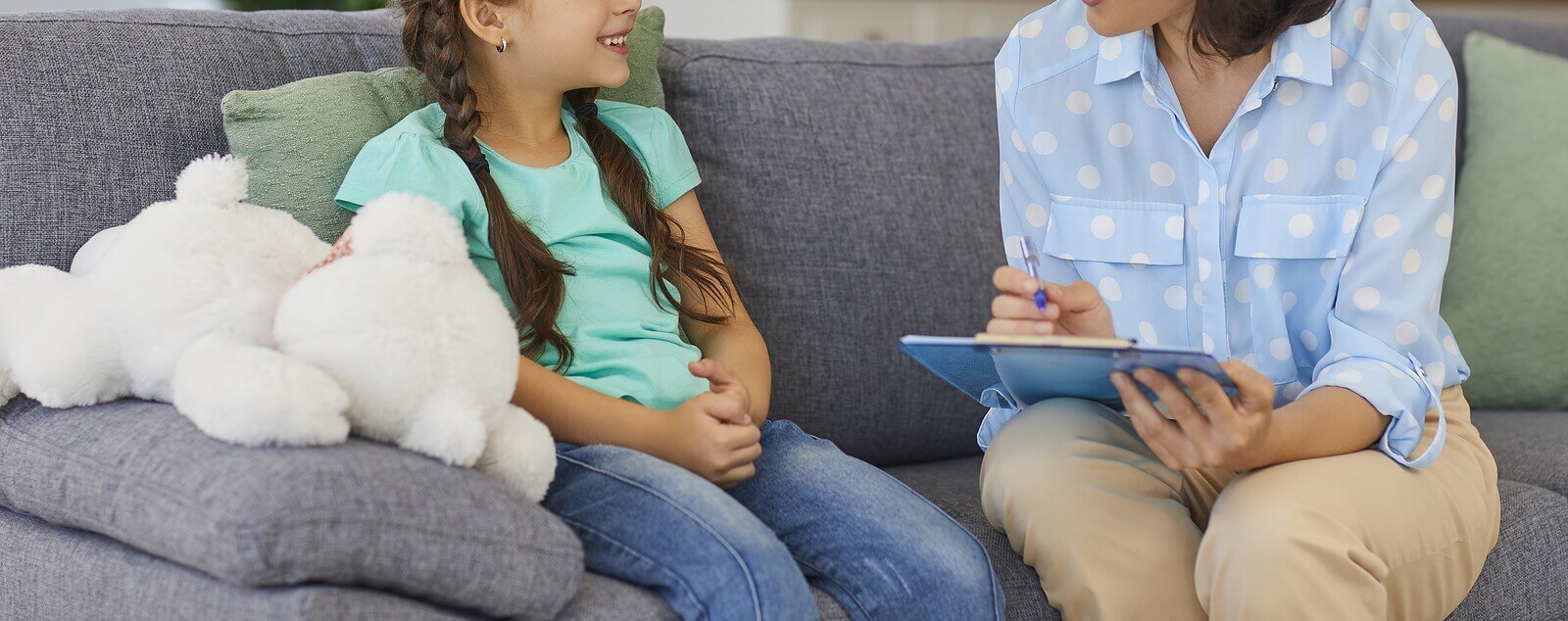 Photo of a young girl sitting on a couch smiling and speaking with an adult woman who is holding a clipboard. Uncover what might be causing your child's learning disability with the help of child neuropsych testing in Saint Petersburg, FL.