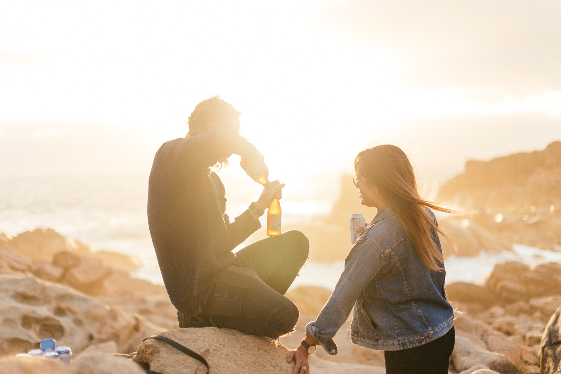 Young interracial couple sitting on the rocks by the beach watching the sunset and having a drink together. A St Petersburg, FL relationship therapist could support you and your partner to improve intimacy and communication. Our expert therapist can help you on your journey to happiness.