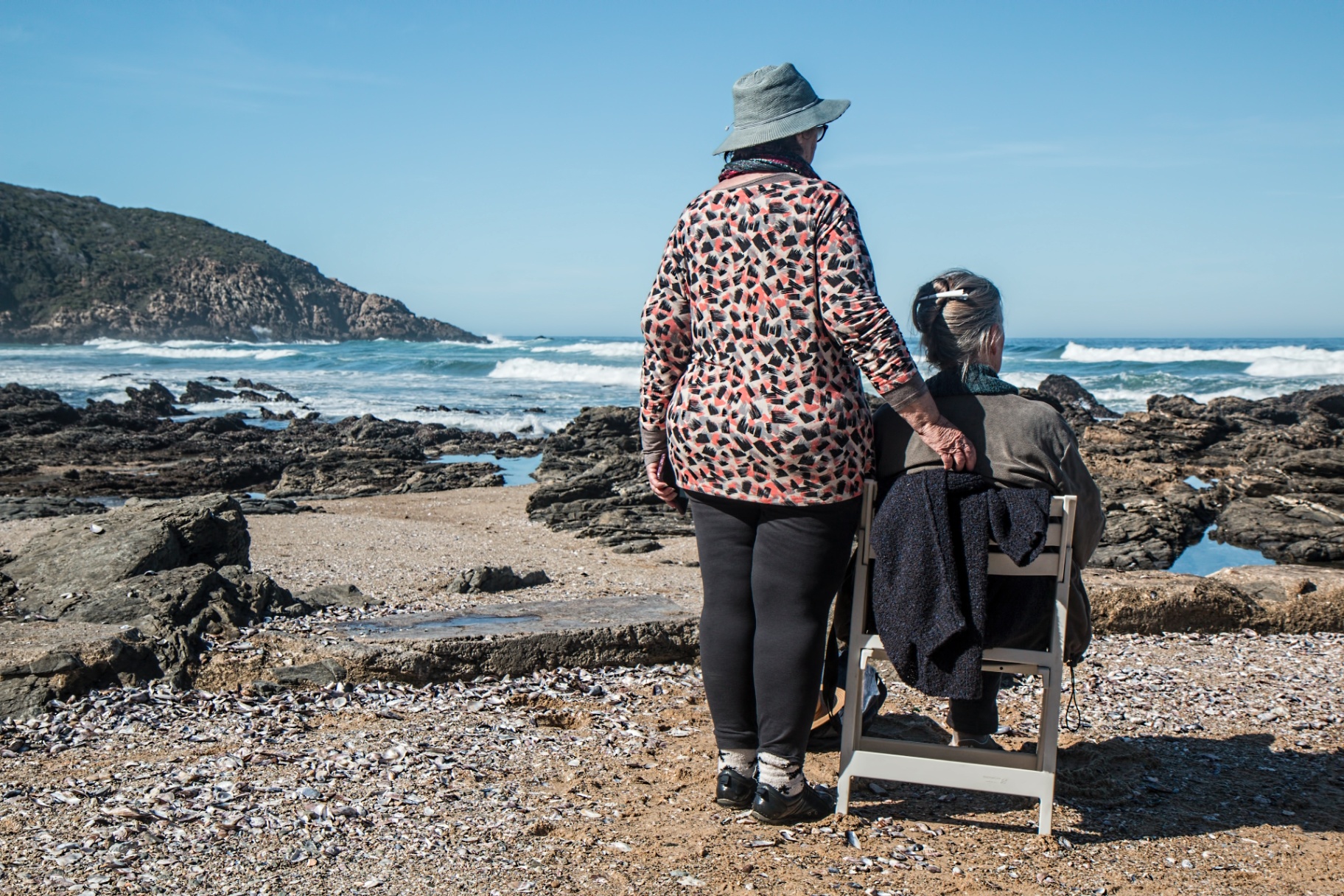 Image of two older women sitting and standing on a rocky beach by the ocean. Uncover your memory issues or problems with the help of adult neuropsychological testing in Saint Petersburg, FL.