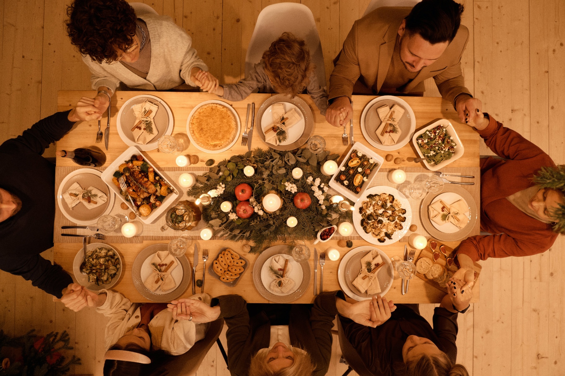 Image of a family sitting around a table full of food holding hands. Discover how to effectively manage your holiday anxiety and how anxiety therapy in Saint Petersburg, FL can provide extra support.
