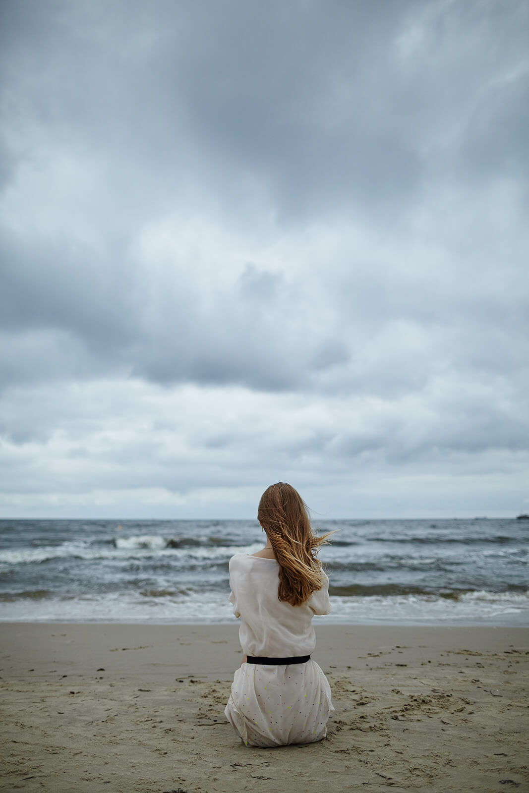 Image of a woman sitting on a sandy beach during a stormy day. Discover how to effectively manage your anxiety symptoms with the help of anxiety therapy in Saint Petersburg, FL.
