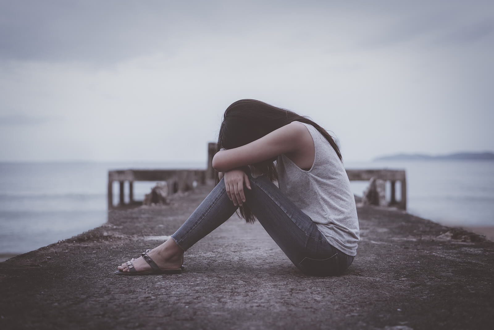 Image of an upset woman sitting on a pier resting her head on her knees. Discover how to effectively cope with your PTSD symptoms with the help of PTSD treatment in Saint Petersburg, FL.