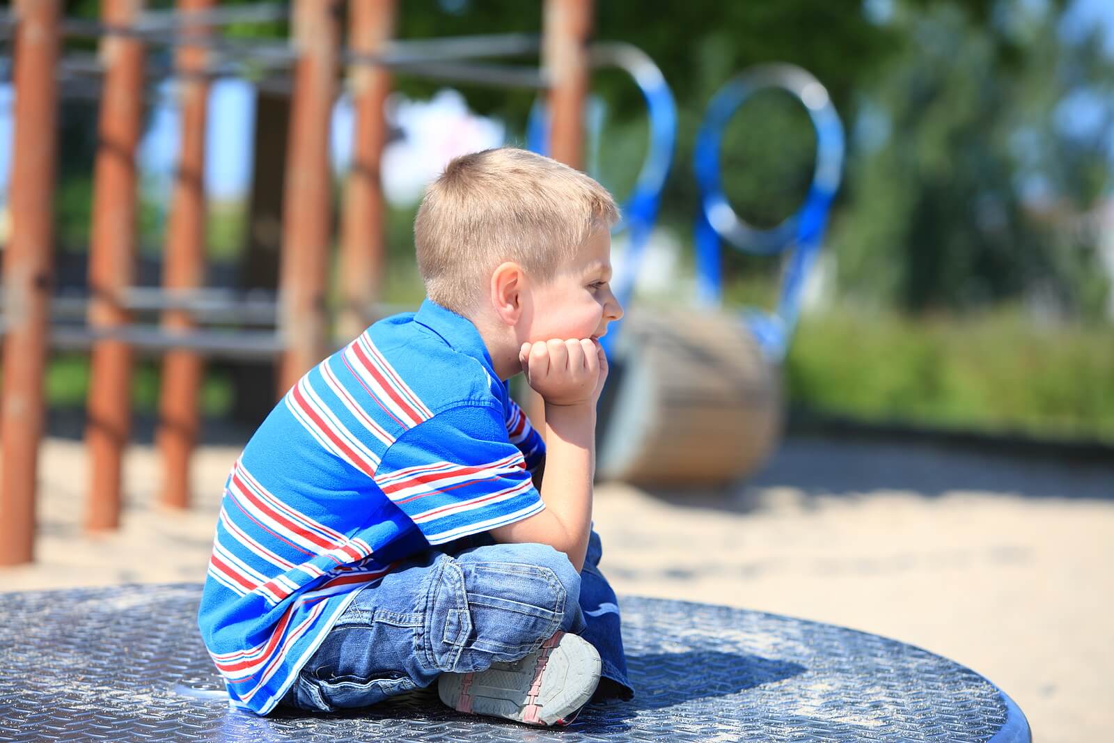 Image of a thoughtful boy sitting on a playground resting his head on his hands. Discover how grief counseling in Saint Petersburg, FL can help your child cope with their emotions.