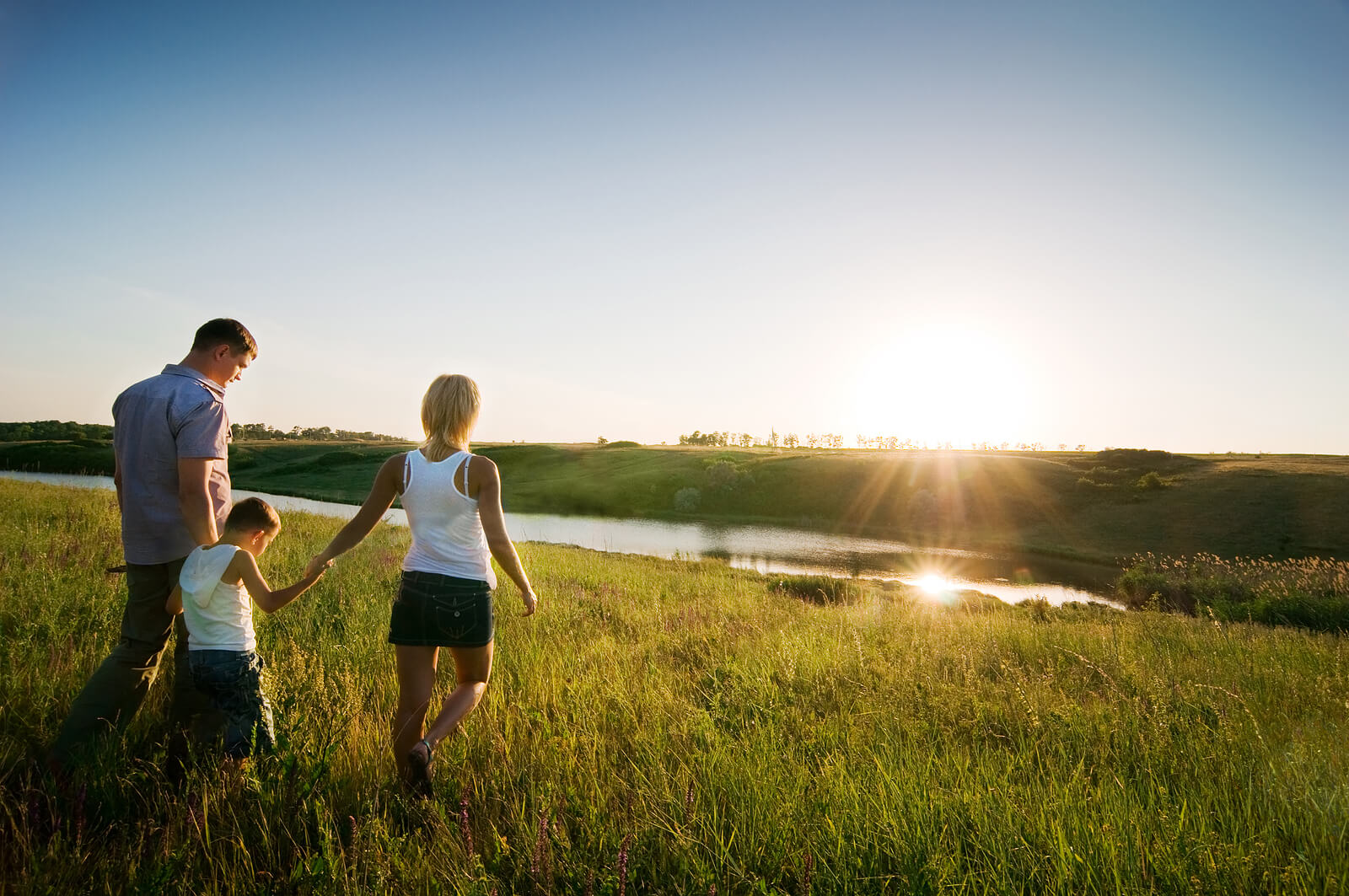 Image of a happy family walking through a field during sunset. If your child is dealing from the loss of a loved one, learn how they can begin to cope in positive ways with grief counseling in Saint Petersburg, FL.
