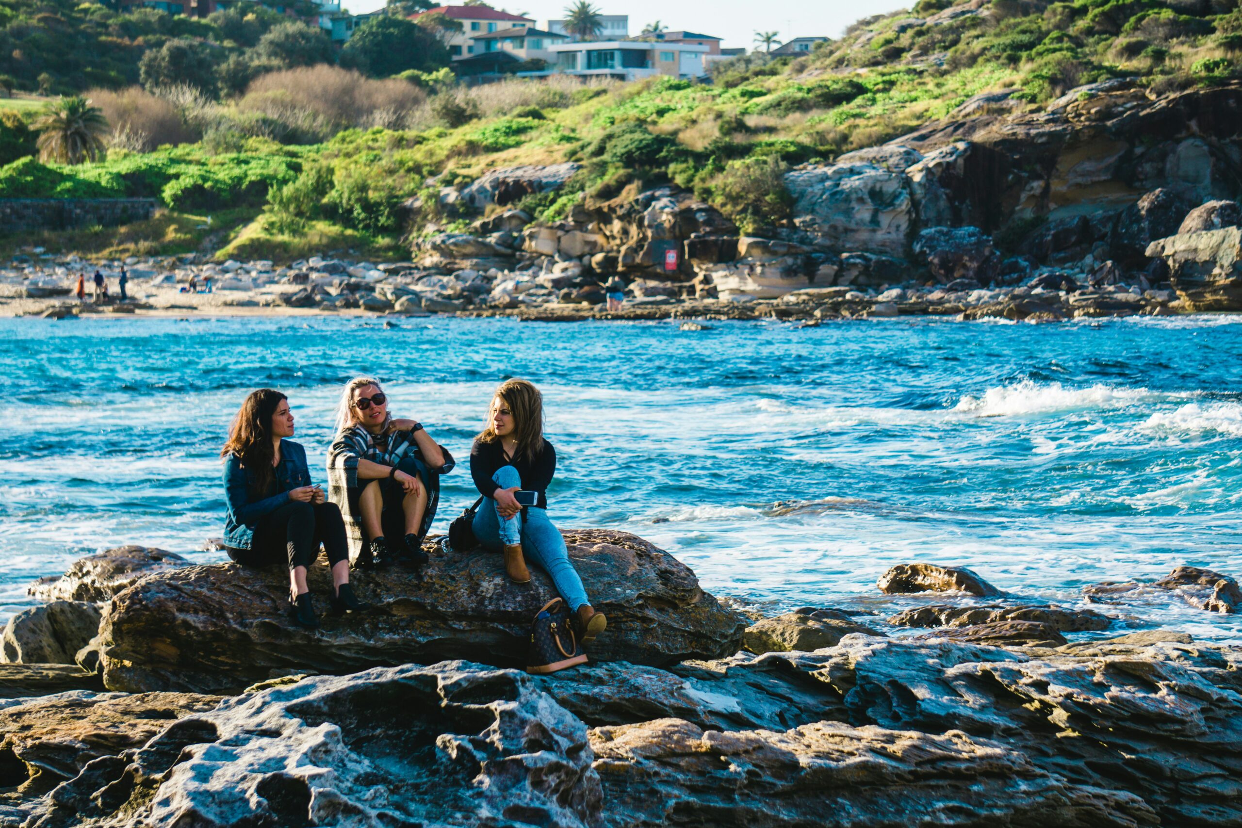 Three sibling teens sitting on a rock by the beach. Looking for a family therapist to help your children reconnect? Call today for support in St Pete, FL.