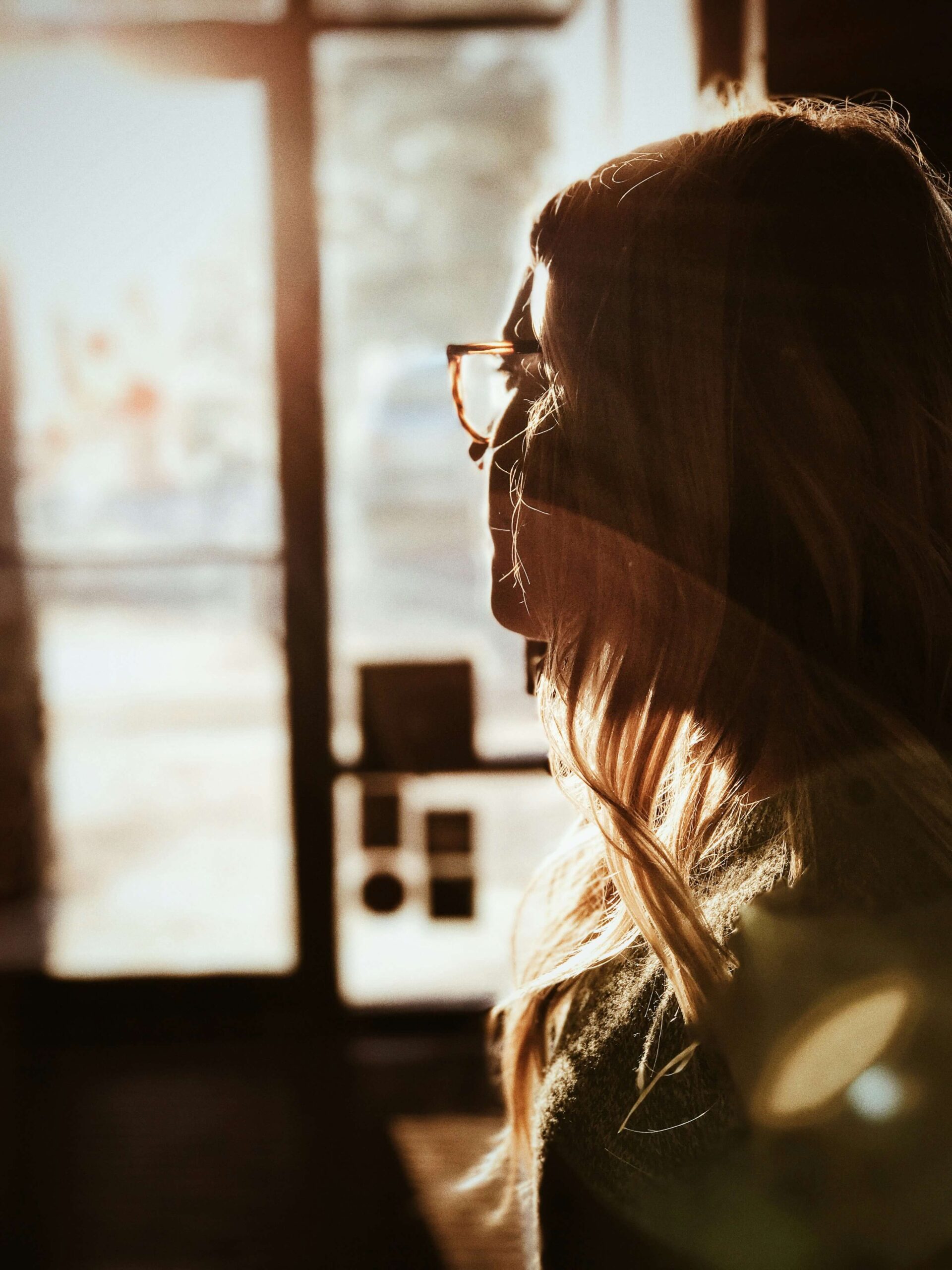 Image of a woman staring out a window while the sun shines on her face. If you struggle with memory loss due to trauma learn how trauma therapy in Saint Petersburg, FL can help.