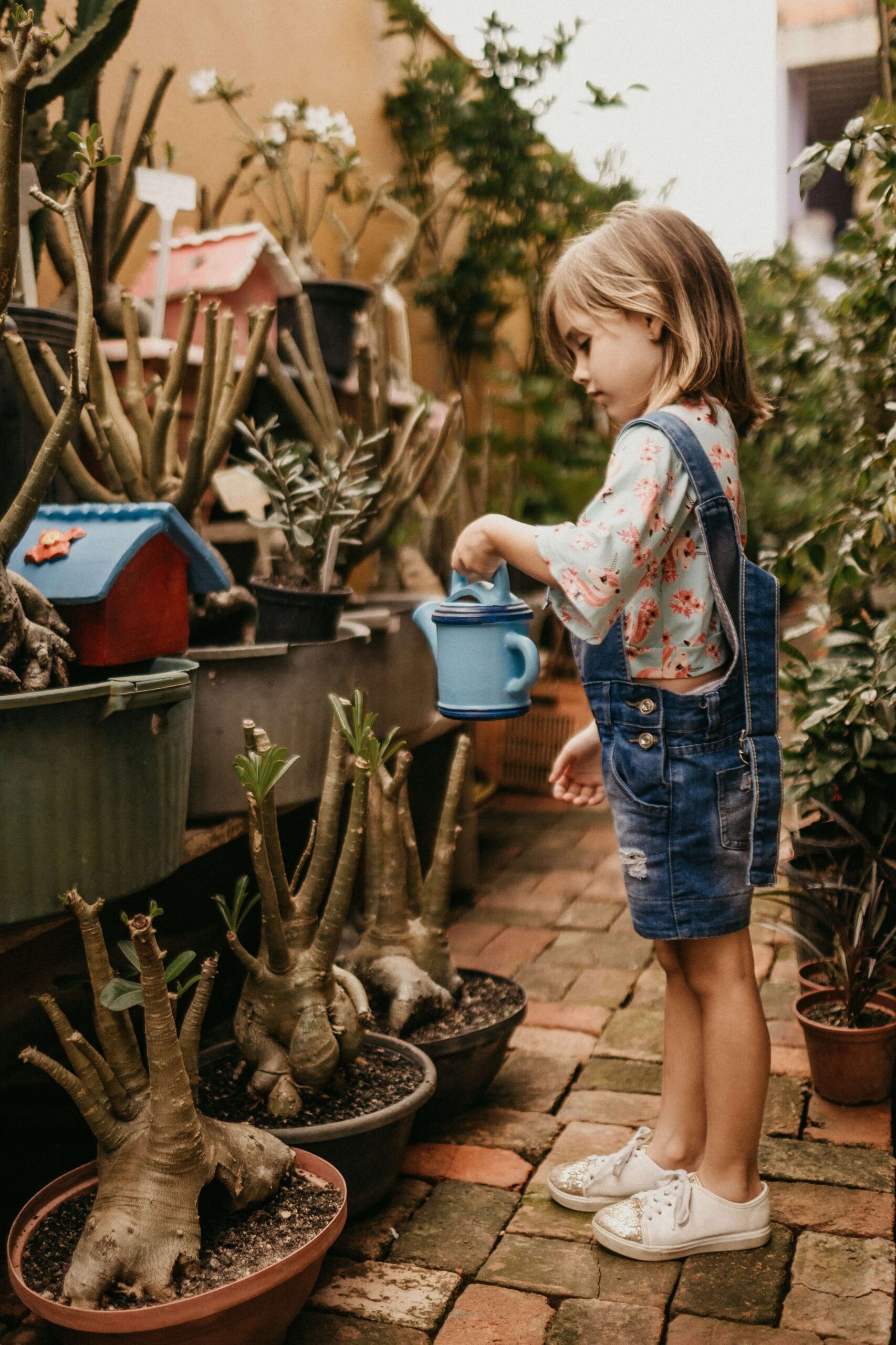 Image of a small girl watering plants with a blue watering can. Help your child effectively cope with anxiety by working with a therapist in anxiety therapy in Saint Petersburg, FL.